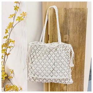 Detailed view of white hand-woven tote bag with hollow floral patterns and tassels