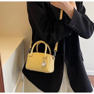 Detail of a bright yellow mini boston bag with litchi texture and silver padlock charm
