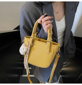 Detail view of bright yellow litchi grain leather bucket bag with cute bear charm