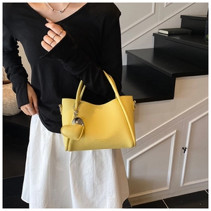 Detailed view of yellow lychee leather handbag featuring a heart-shaped charm and logo