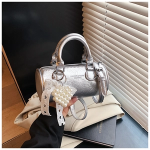 Detail of silver cylindrical handbag with metallic texture, lace bow and pearl heart charm