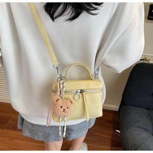 Crossbody bucket bag in pale yellow featuring wrinkled texture and a brown plush bear charm