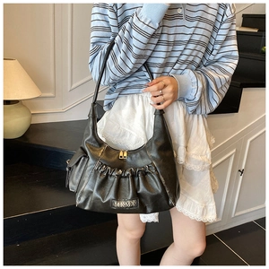 Detail view of the black pleated crescent bag featuring MKMX metal logo and side pockets
