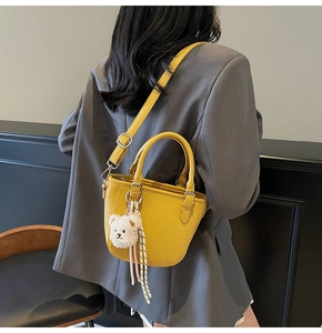 Detail of yellow lychee grain leather bucket bag with a cute plush bear pendant accessory