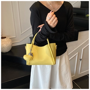 Close-up of bright yellow bucket bag featuring litchi texture and a heart-shaped charm