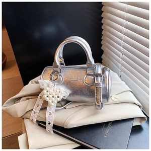 Detail of silver mini Boston cylinder bag with pearl heart charm and lace on a beige blazer