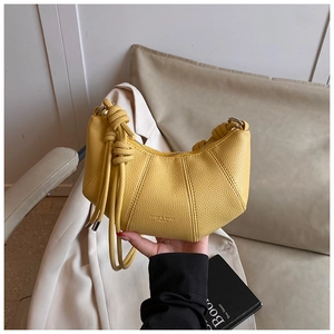 Detail der gelben Halbmond-Tasche mit Lederstruktur und dekorativen Knoten am Schultergurt