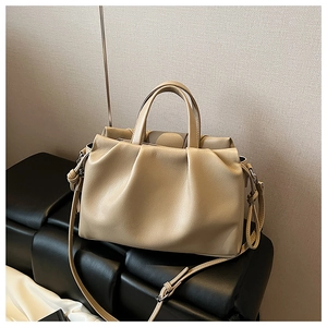 Detailansicht der beigen Eimer-Handtasche mit Falten-Design auf schwarzem Ledersessel