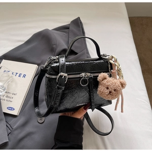 Detail of black glossy wrinkled handbag with teddy bear charm on grey suit background