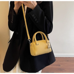 Detail of yellow lychee pattern leather handbag with metallic lock charm and shoulder strap