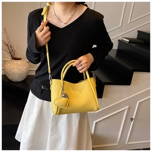 Detail of bright yellow lychee leather handbag with heart charm and shoulder strap