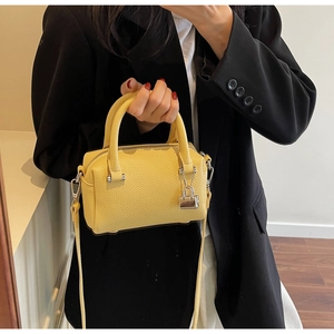 Close-up of a yellow pebbled leather Boston bag held by a model in a black suit