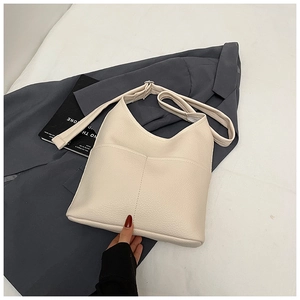 Detail der cremeweißen Beuteltasche mit Lychee-Struktur auf grauem Blazer und Magazin