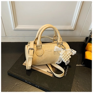 Close-up of cream cylinder bag with glossy texture, pearl heart charm and shoulder strap
