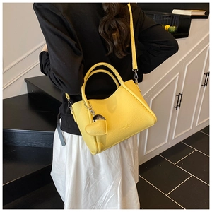 Detail of bright yellow lychee leather handbag featuring a silver heart charm and shoulder strap