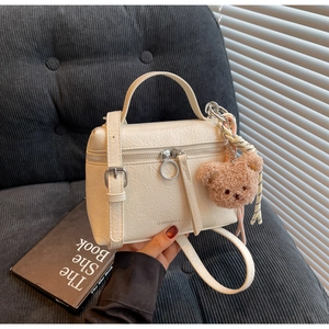 Close-up of cream textured crossbody bag with plush bear charm on grey corduroy
