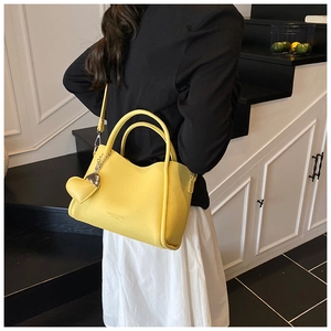Detail view of yellow bucket bag with heart pendant worn on model's shoulder