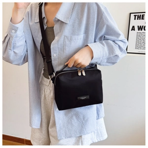 Détail d'un sac bandoulière en nylon noir minimaliste avec logo en métal et double zip