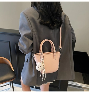 Pink lychee grain leather mini tote bag shown with crossbody strap and cute plush bear charm