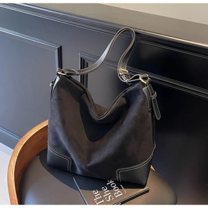 Detail of black suede hobo bag with white contrast stitching on a vintage chair