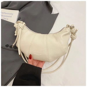 Detail der cremefarbenen Croissant-Tasche mit Kieselleder-Struktur und Knotengurt-Design