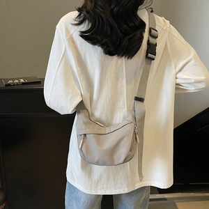 Detail of light grey nylon crescent bag showing metal zippers and wide shoulder strap