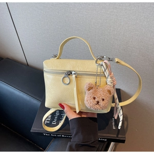 Detailed texture of cream-colored pleated faux leather mini bag with cute bear pendant