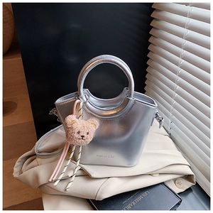 Silver metallic bucket bag with circular handle and brown plush bear charm on a trench coat
