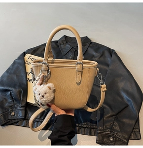 Detail of beige lychee leather bucket bag with plush bear charm and metallic hardware