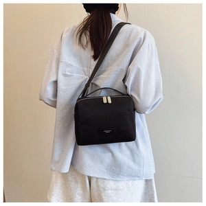 Détail d'un sac bandoulière en nylon noir avec double fermeture éclair et logo métal