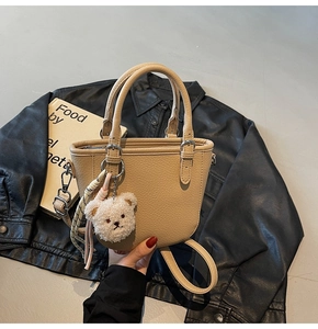 Close-up of beige lychee texture bucket bag with plush bear charm and silk scarf detail