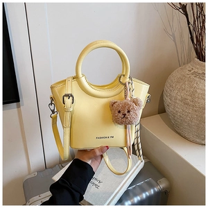 Detail of light yellow bucket bag with metal ring handle and cute plush bear charm