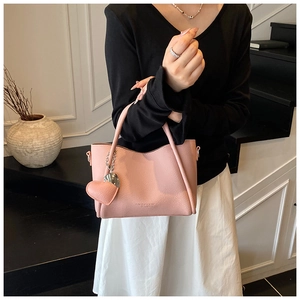 Pink lychee grain leather tote bag with heart charm shown carried by a model