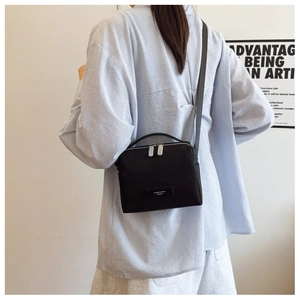 Détail d'un petit sac bandoulière noir avec double fermeture éclair et sangle grise