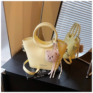 Detail of yellow bucket bag with round handles and a cute plush bear accessory