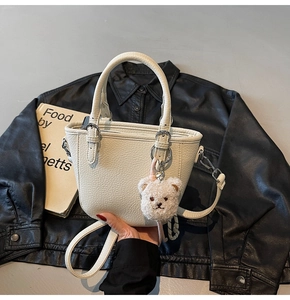 Detail of cream white bucket bag with pebble leather texture and cute plush bear charm