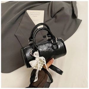 Close-up of black glossy cylinder bag with pleated texture and pearl lace bow detail