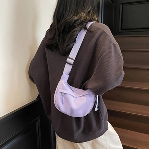Pale purple nylon crescent crossbody bag worn by a model in casual outdoor setting