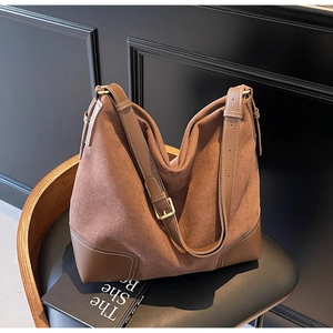 Detail of vintage brown suede tote bag with leather contrast and gold buckle on a chair