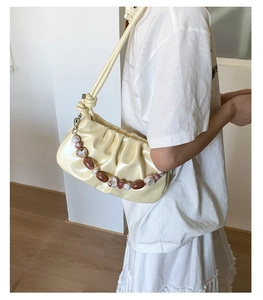 Detail of cream pleated cloud bag with marble bead chain and shoulder strap shown in indoor setting