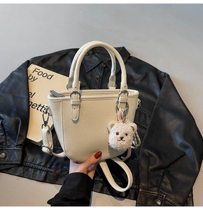Detail of cream lychee leather handbag with plush bear charm on black jacket