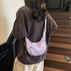 Detailed view of light purple crescent shoulder bag worn on model against wood background