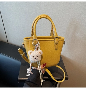 Detail of bright yellow pebbled leather bucket bag with cute white plush bear charm