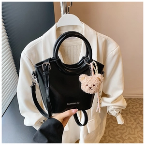 Detail of black bucket bag in patent leather with silk scarf and teddy bear charm