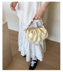 Detail of a creamy yellow pleated cloud bag with a colorful marble bead handle