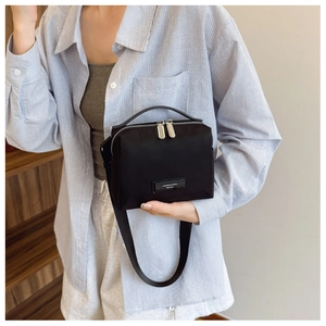 Détail d'un sac bandoulière en nylon noir avec fermeture éclair argentée et plaque logo