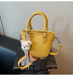 Detail of yellow lychee grain leather bucket bag featuring a cute plush bear pendant accessory