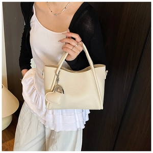 Detail of creamy white pebble leather tote bag with a heart-shaped charm and metal ring