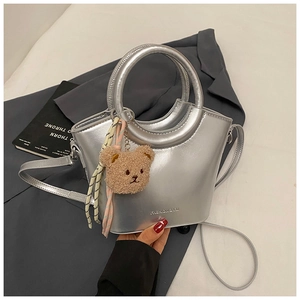 Close-up of silver bucket bag with plush bear charm on a dark grey blazer background