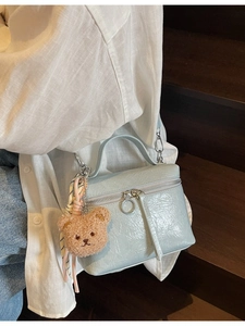 Light blue pleated crossbody bucket bag with bear charm shown on a casual model